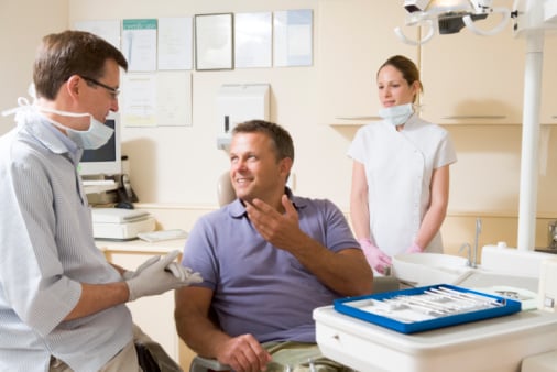 84469771_Dentist_and_assistant_in_exam_room_with_man_in_chair_smiling