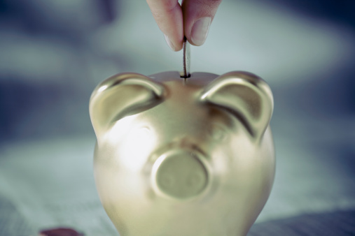 126530543_Persons_hand_putting_coin_into_a_piggy_bank