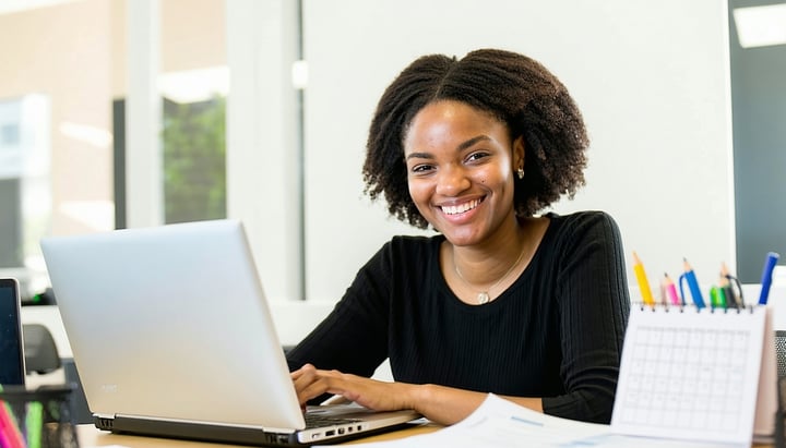 A smiling person looking at their laptop with a calendar and documents on the desk-4