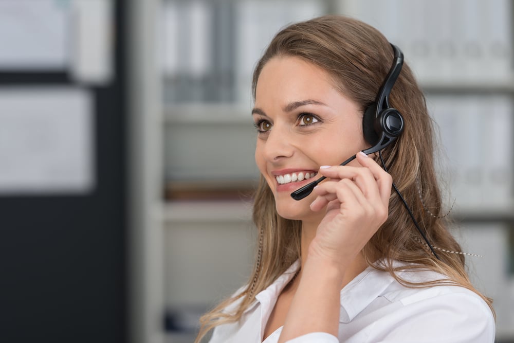 Attractive young client services assistant with a lovely smile listening to a customer on her headset as she offers assistance