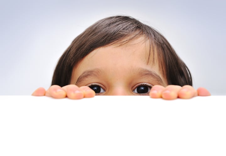 Child holding an empty sign over a white background, hiding behind, copy space