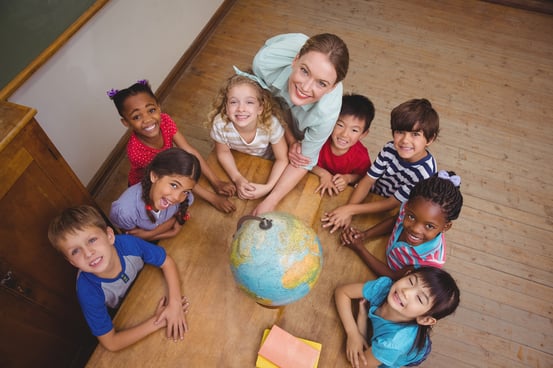 Cute pupils smiling around a globe in classroom with teacher at the elementary school