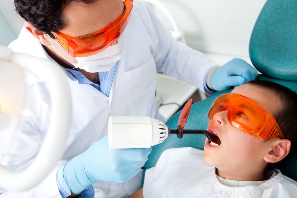 Dentist fixing a cavity on a boy using the laser light