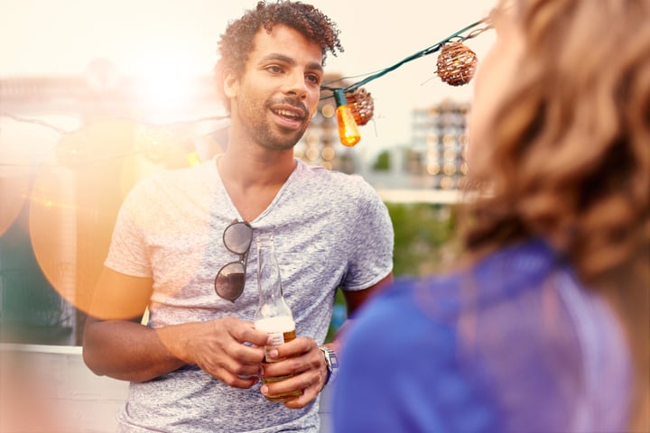 Multi-ethnic millenial couple flirting while having a drink on rooftop terrasse at sunset