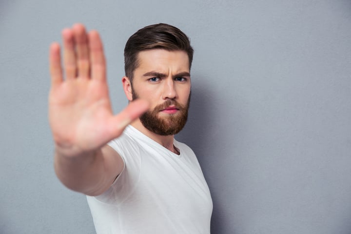 Portrait of a casual man showing stop sign over gray background
