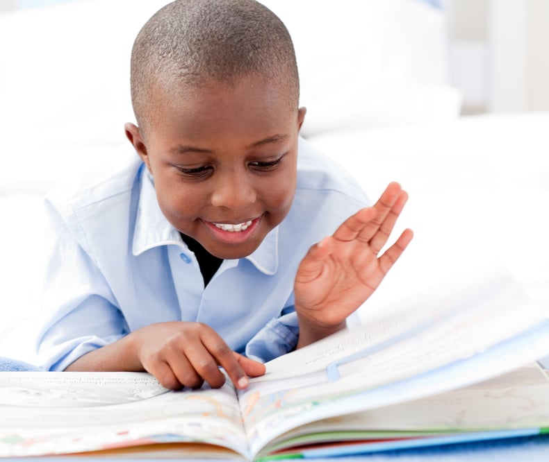 Small boy reading a book on his bed