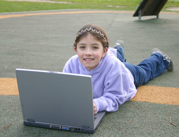 beautiful little girl using a laptop at the playground
