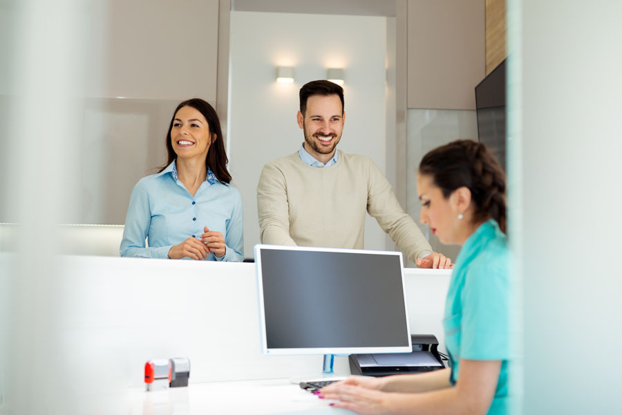 Two smiling people at the front desk of a dentist office