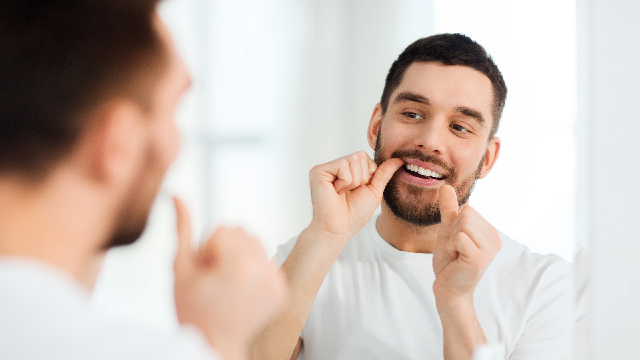 Smiling man flossing his teeth in the mirror