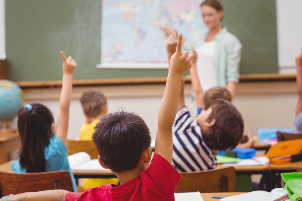 kids in a class room raising hands