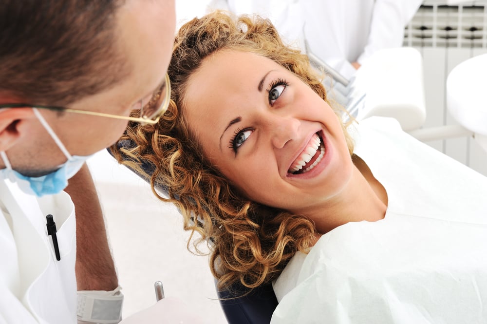 Image of a smiling patient in a chair looking at their dentist