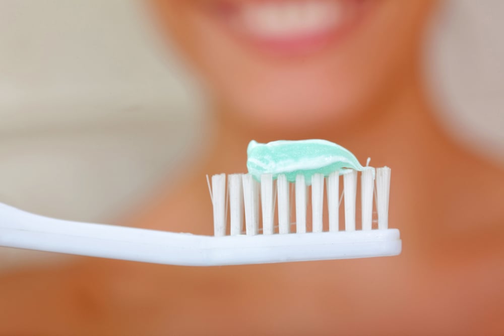 A close-up of a toothbrush with a smiling woman in the background