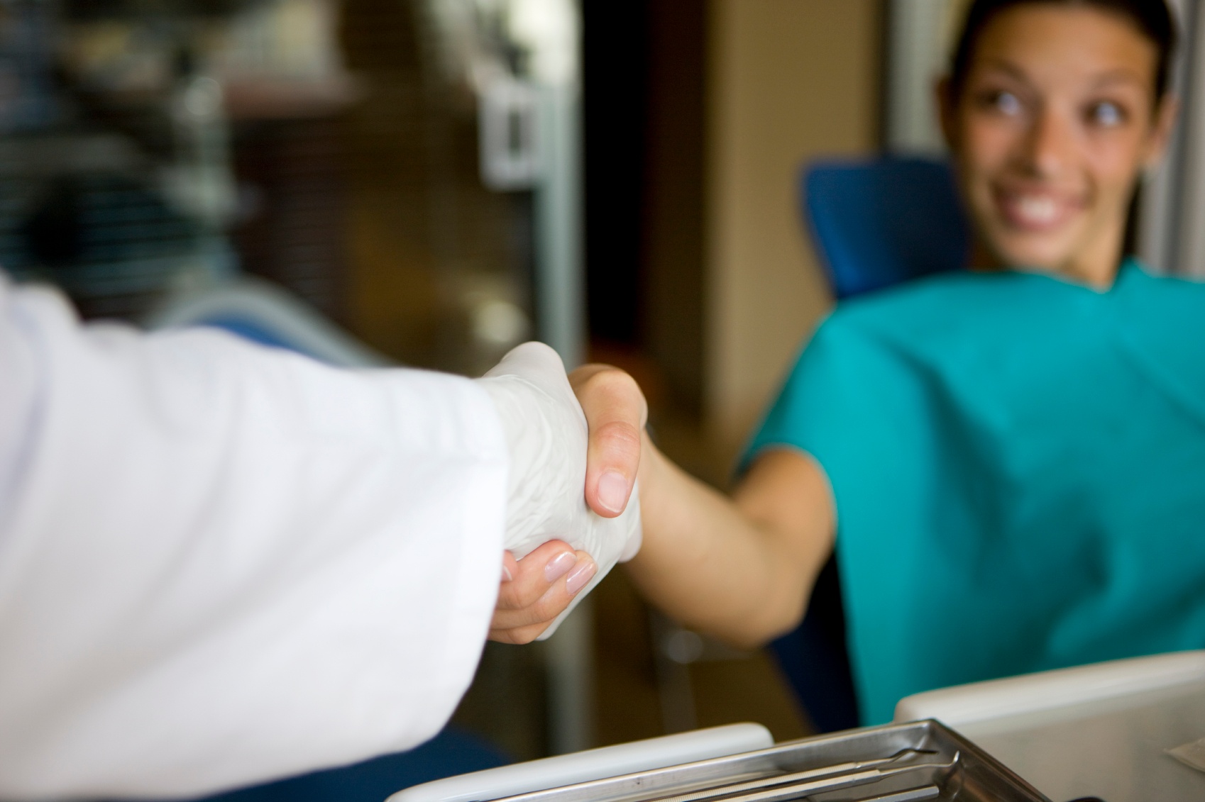 a female patient shaking hands with a dentist wearing gloves